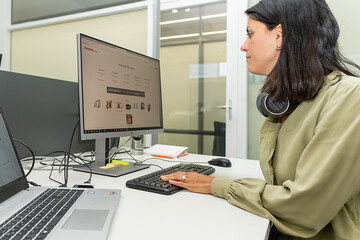 Büroarbeitsplatz mit Mitarbeiterin bei der Arbeit am Computer.
